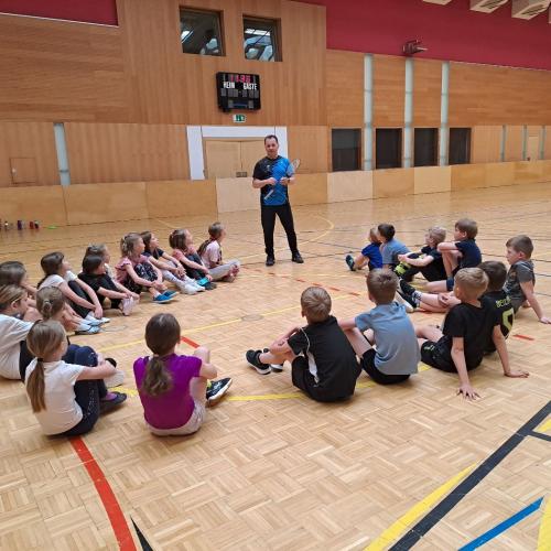 Kinder in der Turnhalle erhalten eine Erklärung von einem Tennistrainer.