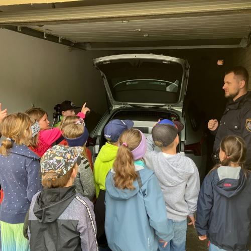 Ein Polizist erklärt den Kindern, was alles in einem Polizeiauto ist und zeigt es ihnen.