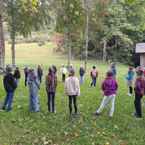 Kinder stehen im Kreis auf einer Wiese und erhalten eine Erklärung zum Slacklinen.