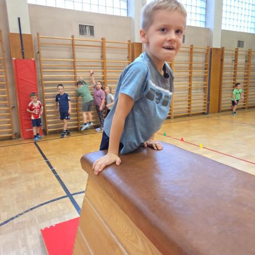 Kinder springen auf den Kasten im Turnsaal.