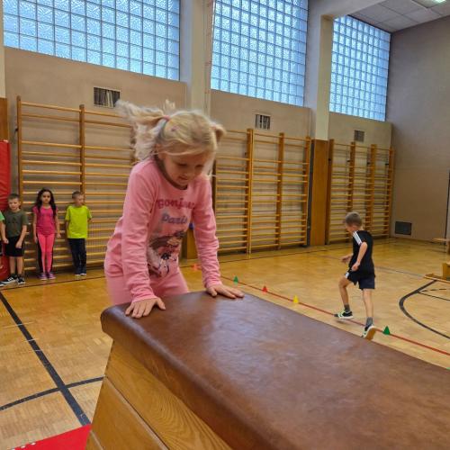 Kinder springen auf den Kasten im Turnsaal.