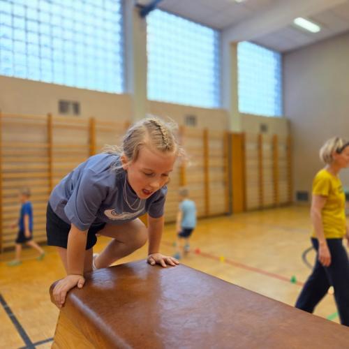 Kinder springen auf den Kasten im Turnsaal.