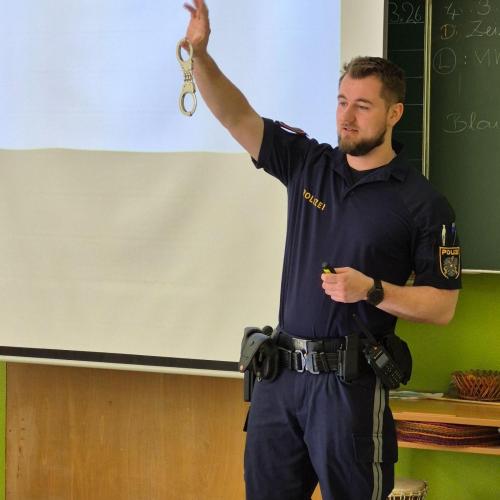 Der Polizist zeigt den Kindern Handschellen.