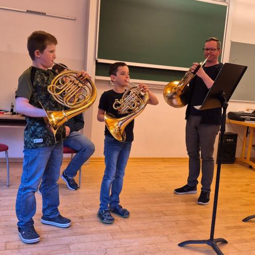 Ein Lehrer spielt mit seinen Schülern auf den Flügelhörnern etwas vor.