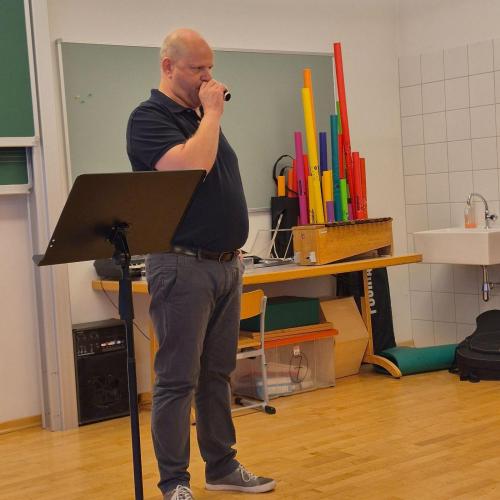 Ein Lehrer bläst durch ein Mundstück eines Instruments.