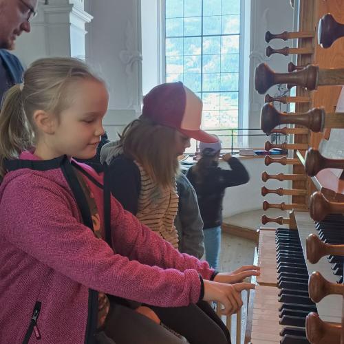 Kinder sitzen auf der Orgelbank und dürfen Orgel spielen.