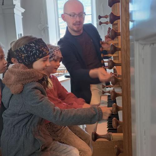 Kinder sitzen auf der Orgelbank und dürfen Orgel spielen.