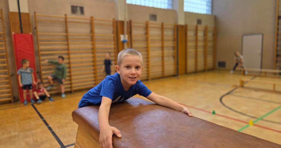 Kinder springen auf den Kasten im Turnsaal.